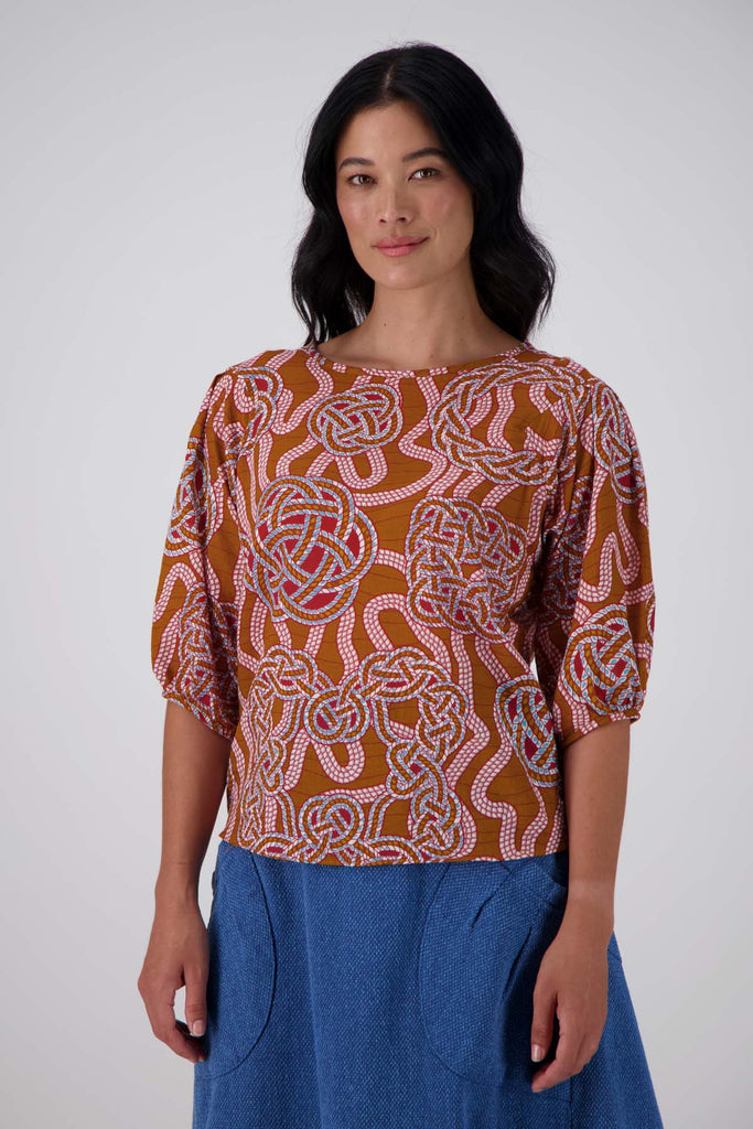 Olga de Polga seersucker blouse in the Love knots print with deep caramel brown and accents of blue and red. Wide boatneck neckline and back zip fastening. Front view on model.