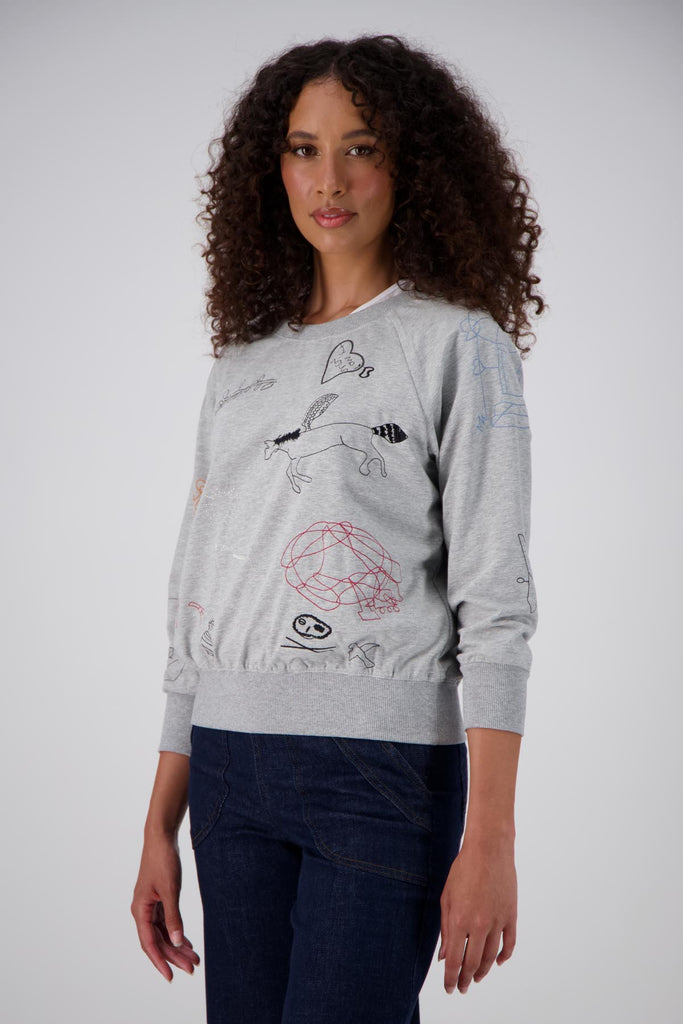Grey Olga de Polga Montage Sweater in a soft brushed cotton tencel blend. The sweatshirt features abstract embroidered motifs on the front and arms. The sweatshirt has ribbing at the neck, cuffs and hem. This is lightweight and a perfect layering sweater. Side front view