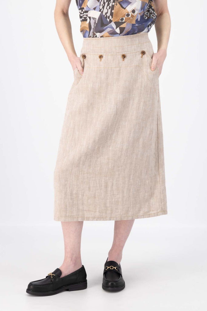 Olga de Polga Hepburn skirt in herringbone linen. Colour beige. Featuring a unique button detail at the waist that forms a flattering pocket shape, this skirt adds personality to any outfit. With an elasticated back waist for comfort, it finishes just below the knee and has a stylish back split for ease of movement. Front close view on model.