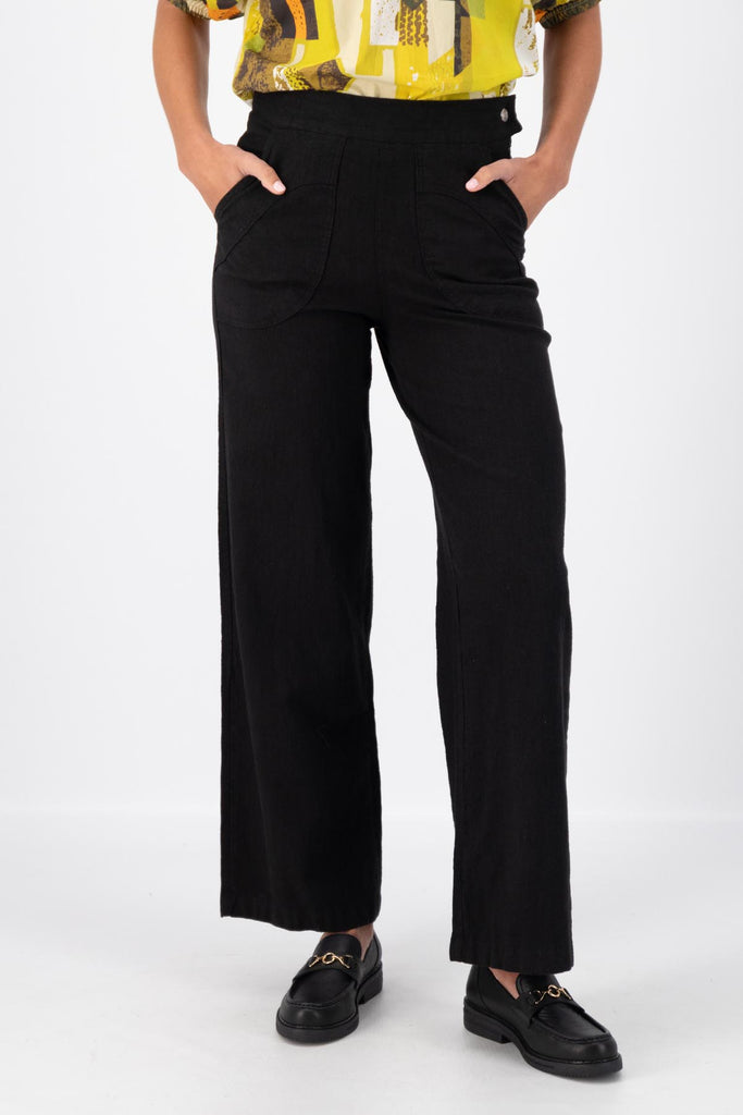 Olga de Polga Peggy Pants Long Lino in Black linen. Featuring a flattering high waist with an elasticated back, these pants provide all-day comfort while maintaining a sleek, streamlined look. With their stretchy wide-leg fit, flat front, and full-length silhouette, they effortlessly elevate any outfit. Front close-up view on model.