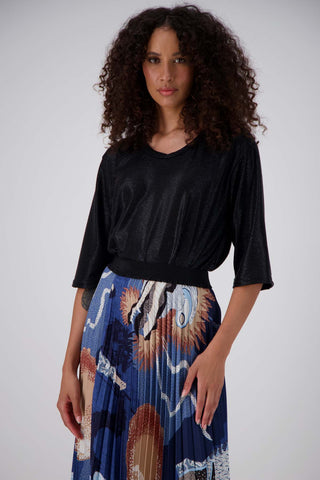 Olga de Polga Black Prosecco top in metallic polyester fabric. With a relaxed fit, scoop neckline, and 3/4 length sleeves, your everyday t-shirt now boasts a lustrous twist. Front close view on model, tucked into a skirt.