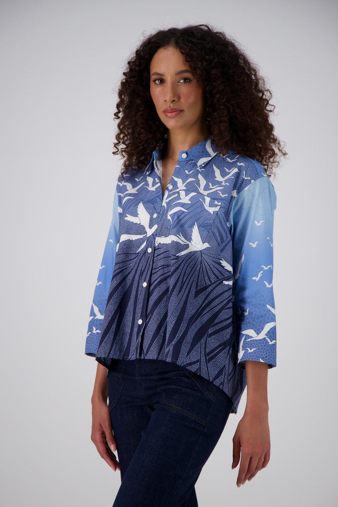 Olga de Polga Blue Homebound printed cotton shirt. With 3/4 length sleeves and a collar with a button down front, this shirt has an oversized fit with a trapeze shape. Waist length at the front with the back is hip length creating a lovely drape. Front close up view on model.