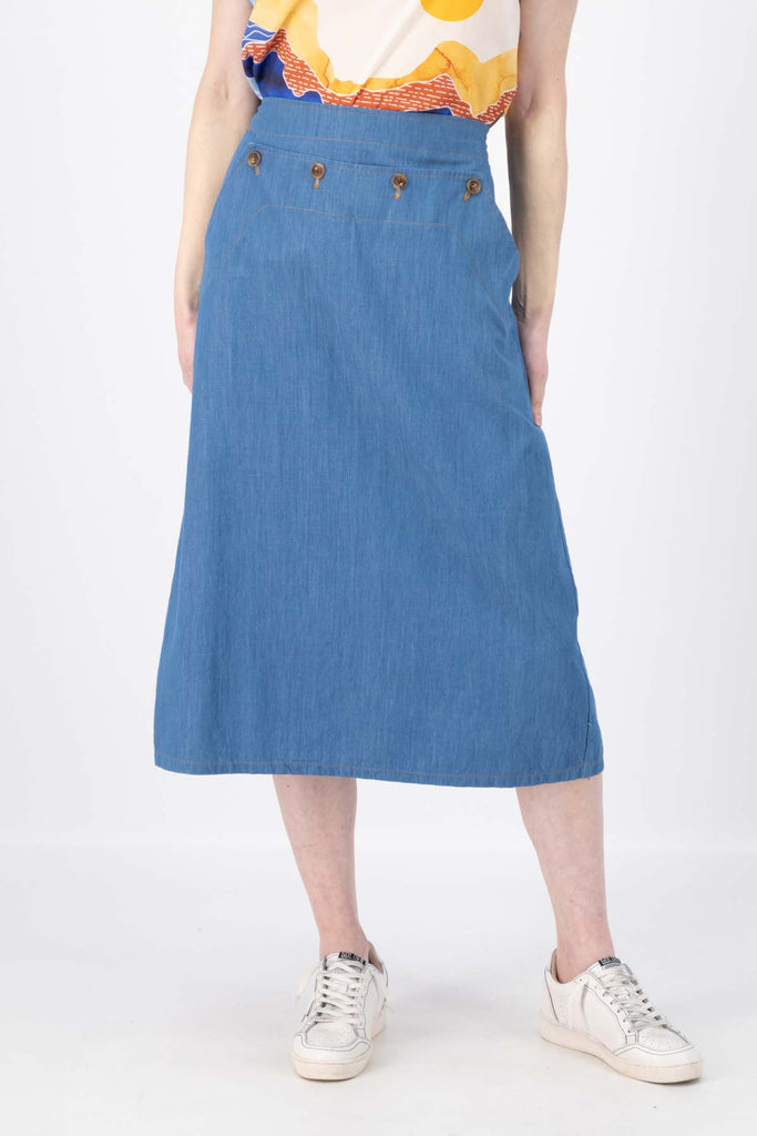 Olga de Polga Hepburn skirt in light wash cotton denim. The Hepburn Skirt is a chic pencil skirt with a playful twist. Featuring a unique button detail at the waist that forms a flattering pocket shape. Front close-up view on model.