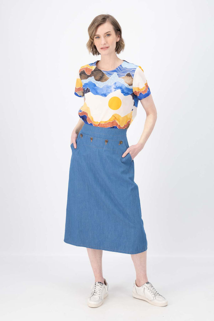 Olga de Polga Hepburn skirt in light wash cotton denim. The Hepburn Skirt is a chic pencil skirt with a playful twist. Featuring a unique button detail at the waist that forms a flattering pocket shape. Front view on model.