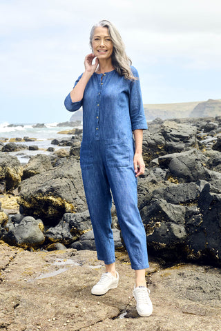 Olga de Polga Blue mid-wash denim Artisan Jumpsuit in cotton denim. Half sleeves and a button down front with patch pockets. Ankle length.  front full length view on model outdoors