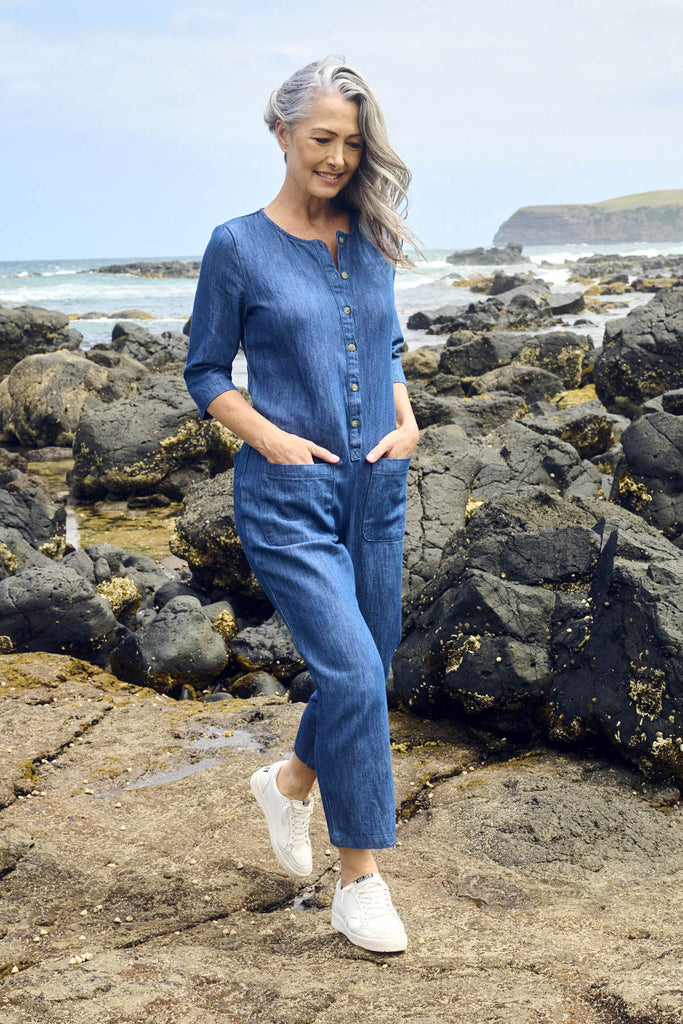 Olga de Polga Blue mid-wash denim Artisan Jumpsuit in cotton denim. Half sleeves and a button down front with patch pockets. Ankle length.  Side front view on model