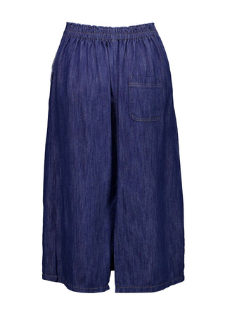 Olga de Polga mid-wash denim Hepburn Skirt. A pencil skirt with a twist.  Featuring a unique button detail at the waist that forms a flattering pocket shape, this skirt adds personality to any outfit. With an elasticated back waist for comfort, it finishes just below the knee and has a stylish back split for ease of movement. Back view.