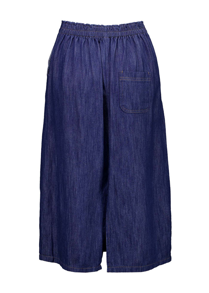 Olga de Polga mid-wash denim Hepburn Skirt. A pencil skirt with a twist.  Featuring a unique button detail at the waist that forms a flattering pocket shape, this skirt adds personality to any outfit. With an elasticated back waist for comfort, it finishes just below the knee and has a stylish back split for ease of movement. Back view.