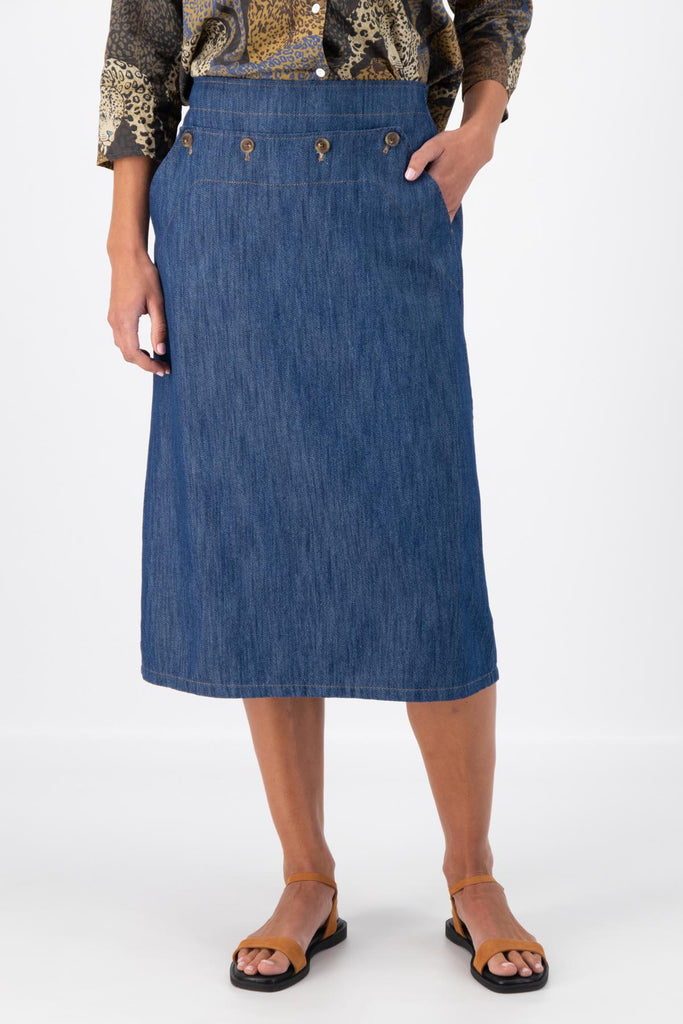 Olga de Polga mid-wash denim Hepburn Skirt. A pencil skirt with a twist.  Featuring a unique button detail at the waist that forms a flattering pocket shape, this skirt adds personality to any outfit. With an elasticated back waist for comfort, it finishes just below the knee and has a stylish back split for ease of movement. Front close-up view on model.