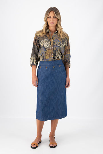 Olga de Polga mid-wash denim Hepburn Skirt. A pencil skirt with a twist.  Featuring a unique button detail at the waist that forms a flattering pocket shape, this skirt adds personality to any outfit. With an elasticated back waist for comfort, it finishes just below the knee and has a stylish back split for ease of movement. Front view on model.