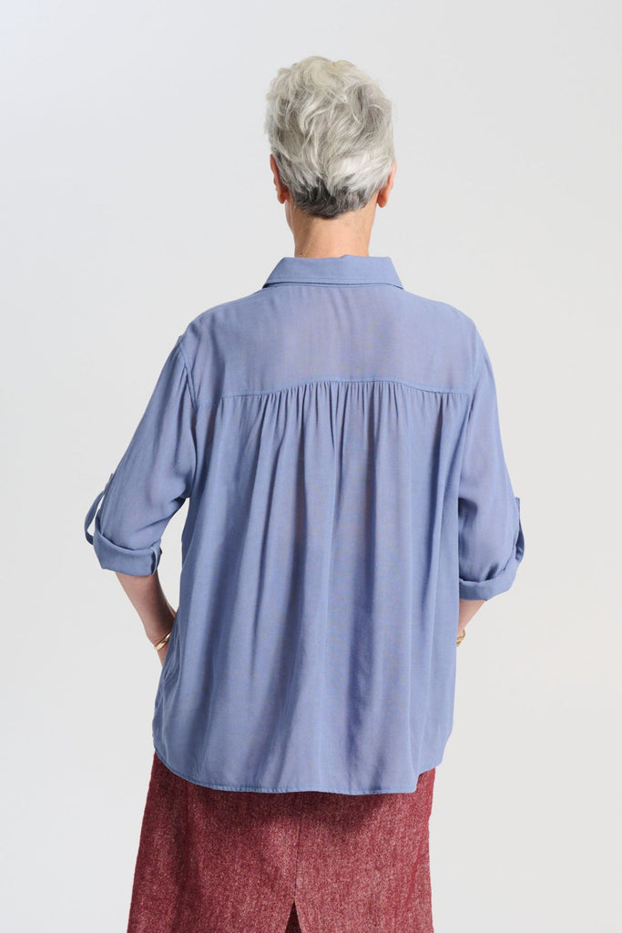Olga de Polga Smokey Blue Ava shirt in mid-weight viscose crepe. With a button down front and collar, 3/4 sleeves with an option to fasten half way up. Front finishes at the waist and the back drapes down lower to the hip. Back view on model