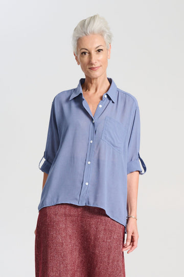 Olga de Polga Smokey Blue Ava shirt in mid-weight viscose crepe. With a button down front and collar, 3/4 sleeves with an option to fasten half way up. Front finishes at the waist and the back drapes down lower to the hip. Front view on model.