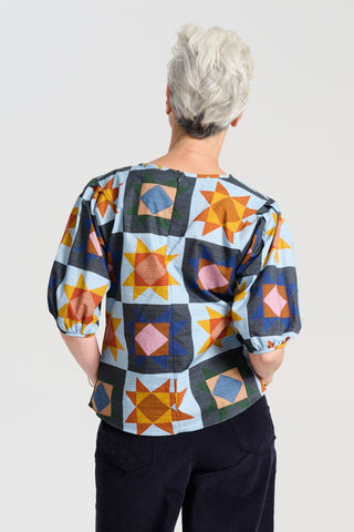 The blouse features a beautifully detailed lantern sleeve with a drop shoulder and delicate pleating on the shoulder and cuff. It also has a wide boat neckline and invisible zip fastening at the back. Back view on model