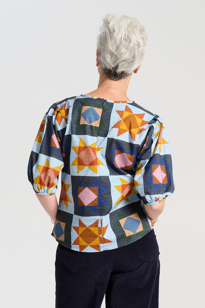 The blouse features a beautifully detailed lantern sleeve with a drop shoulder and delicate pleating on the shoulder and cuff. It also has a wide boat neckline and invisible zip fastening at the back. Back view on model