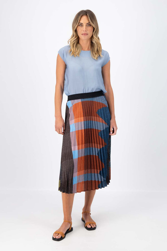 Olga de Polga pleated skirt in the Jada print. Colours of Umber, orange and cobalt blue shine in this print Elasticated waistband. Midi length. Front view on model.