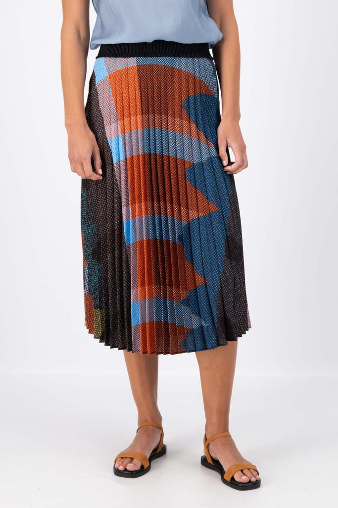 Olga de Polga pleated skirt in the Jada print. Colours of Umber, orange and cobalt blue shine in this print Elasticated waistband. Midi length. Front close-up view on model.