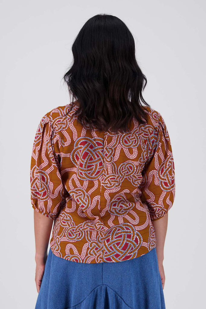 Olga de Polga seersucker blouse in the Love knots print with deep caramel brown and accents of blue and red. Wide boatneck neckline and back zip fastening. Back view