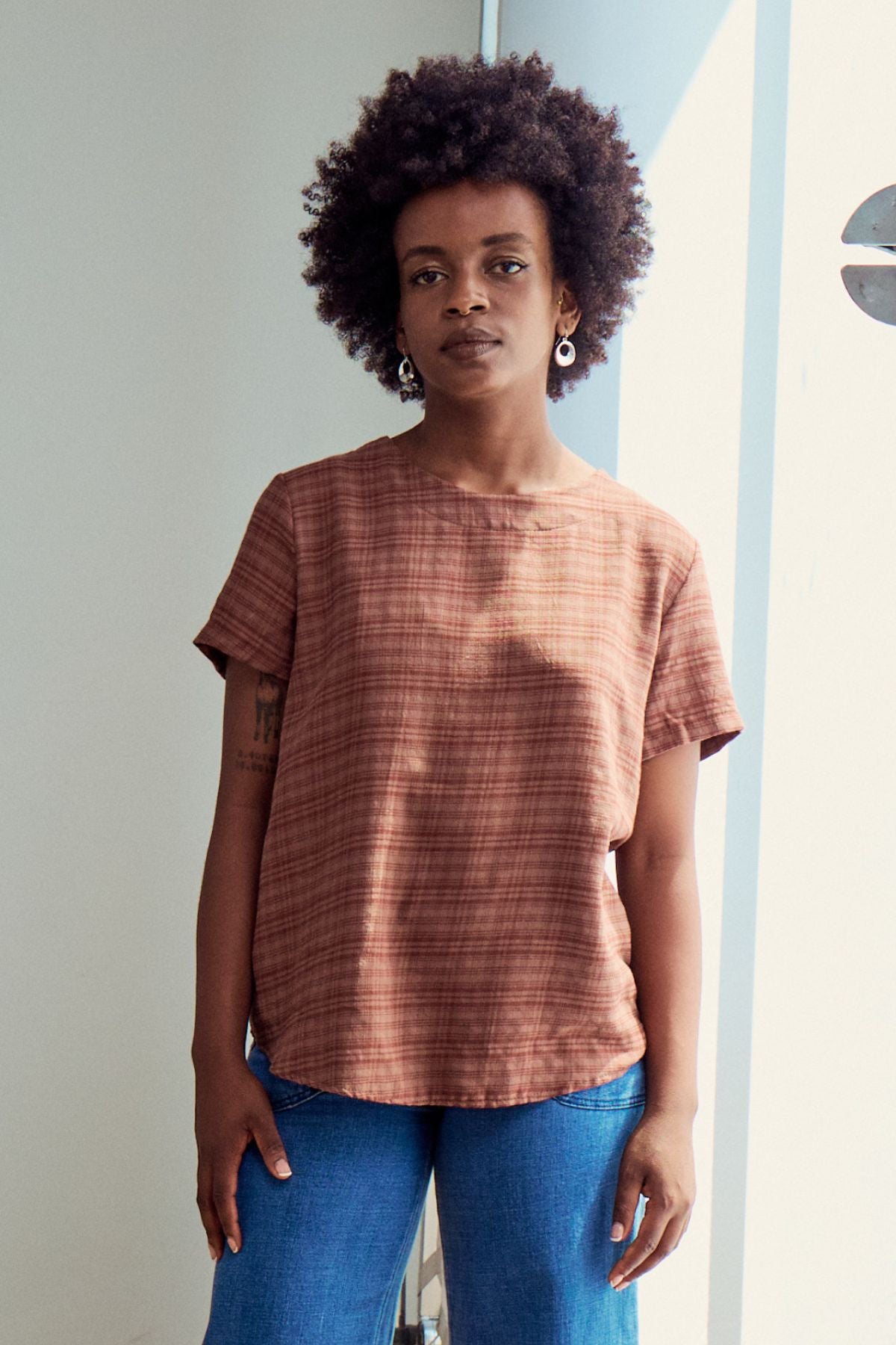 Olga de Polga Mocha brown top in brushed cotton seersucker. A little more modest and roomy than the tee, it is a straight cut, with a short sleeve, crew neck and a box pleat at the back to give it more fullness and movement. Front view on model