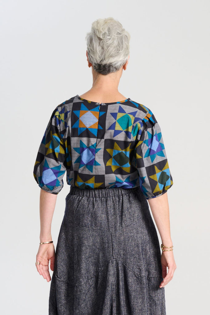 Olga de Polga Veda Blouse Night in printed cotton.  The blouse features a beautifully detailed lantern sleeve with a drop shoulder and delicate pleating on the shoulder and cuff. It also has a wide boat neckline and invisible zip fastening at the back. Back view on model