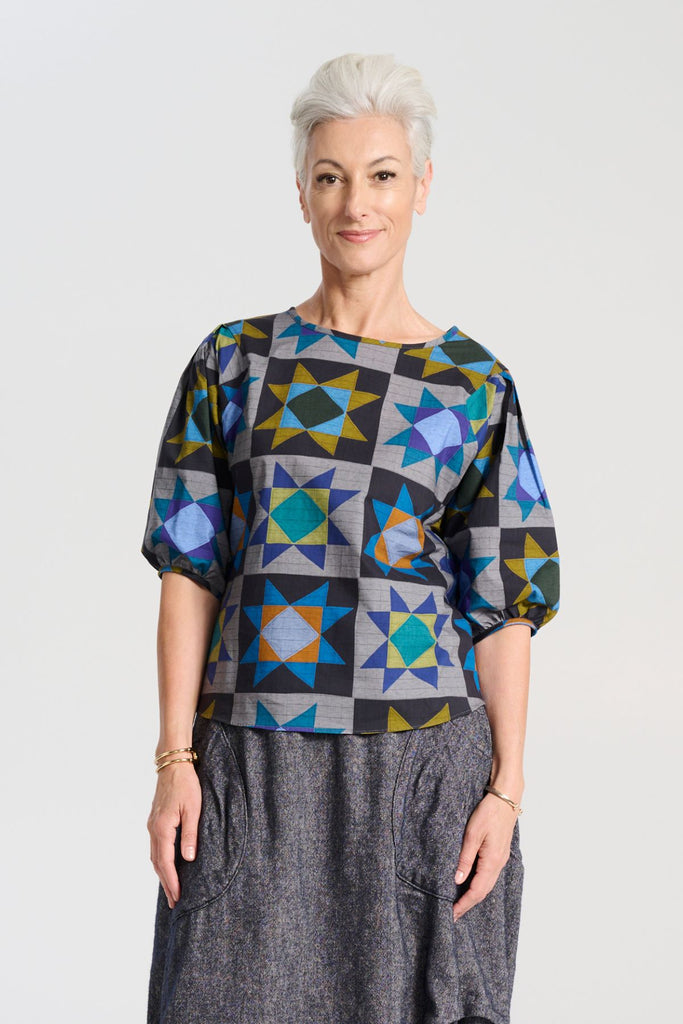 Olga de Polga Veda Blouse Night in printed cotton.  The blouse features a beautifully detailed lantern sleeve with a drop shoulder and delicate pleating on the shoulder and cuff. It also has a wide boat neckline and invisible zip fastening at the back. Front close up view on model