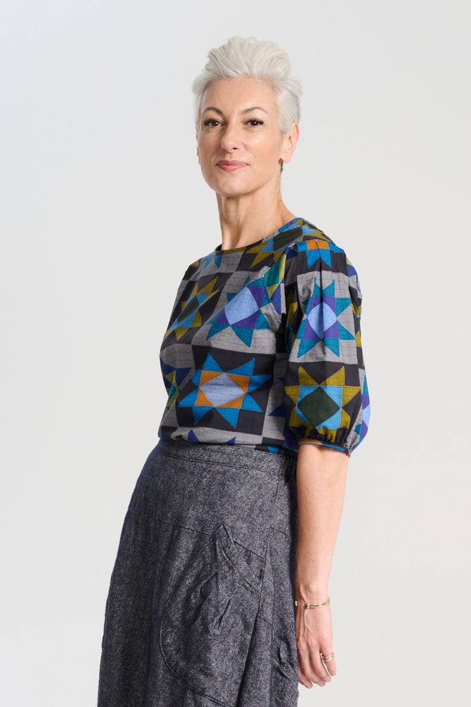 Olga de Polga Veda Blouse Night in printed cotton.  The blouse features a beautifully detailed lantern sleeve with a drop shoulder and delicate pleating on the shoulder and cuff. It also has a wide boat neckline and invisible zip fastening at the back. Side view on model