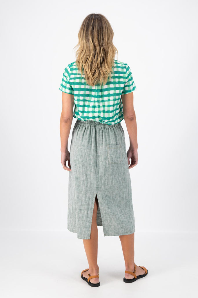 Olga de Polga Green Hepburn skirt in herringbone linen. A pencil skirt with a twist.  Featuring a unique button detail at the waist that forms a flattering pocket shape, this skirt adds personality to any outfit. With an elasticated back waist for comfort, it finishes just below the knee and has a stylish back split for ease of movement. Back view on model.