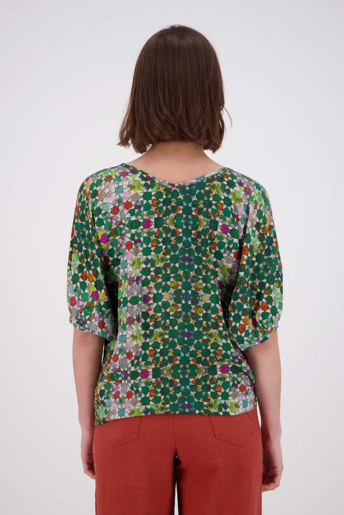 Olga de Polga Kaleidoscope Green Camisa Blouse in printed fine Tencel. This is a reversible top with the choice of a soft V-neck and a boat neck which are interchangeable. Half length sleeves. Finishes at the hip. Back close up view on model.