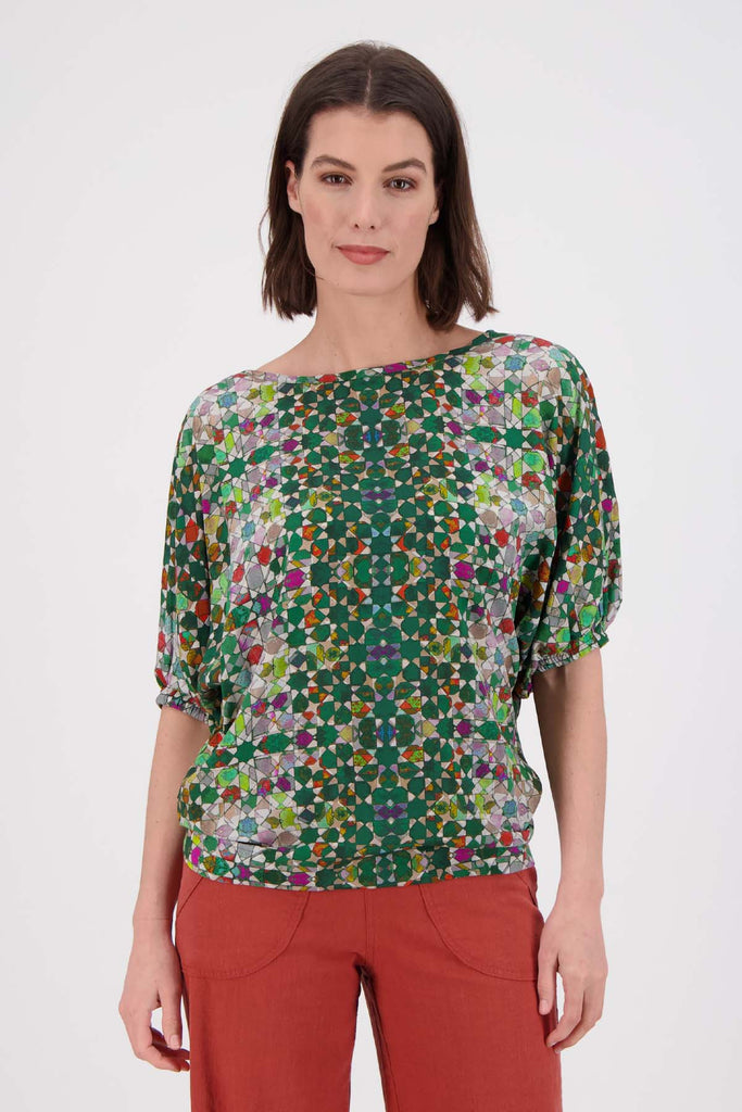 Olga de Polga Kaleidoscope Green Camisa Blouse in printed fine Tencel. This is a reversible top with the choice of a soft V-neck and a boat neck which are interchangeable. Half length sleeves. Finishes at the hip. Front close up view on model.