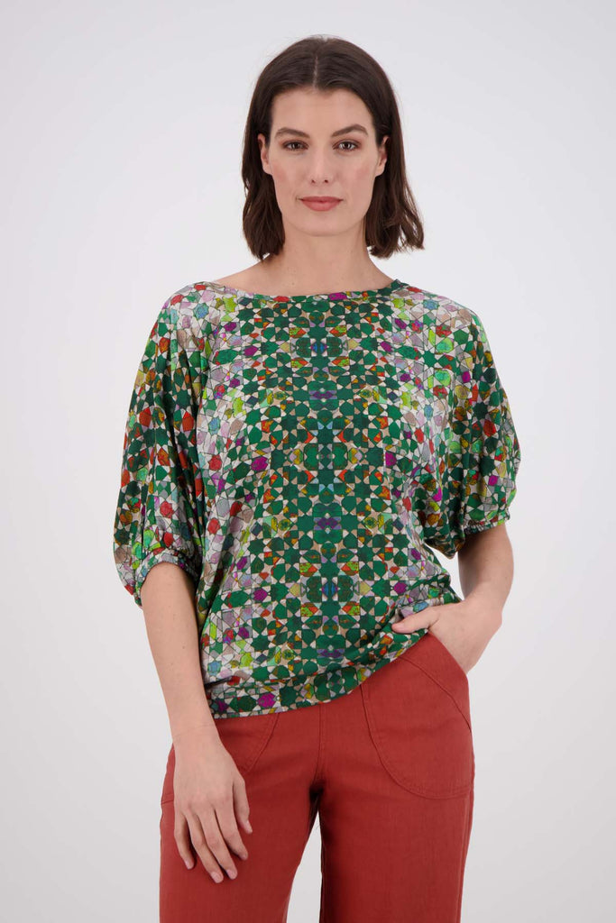 Olga de Polga Kaleidoscope Green Camisa Blouse in printed fine Tencel. This is a reversible top with the choice of a soft V-neck and a boat neck which are interchangeable. Half length sleeves. Finishes at the hip. Front close up view on model.