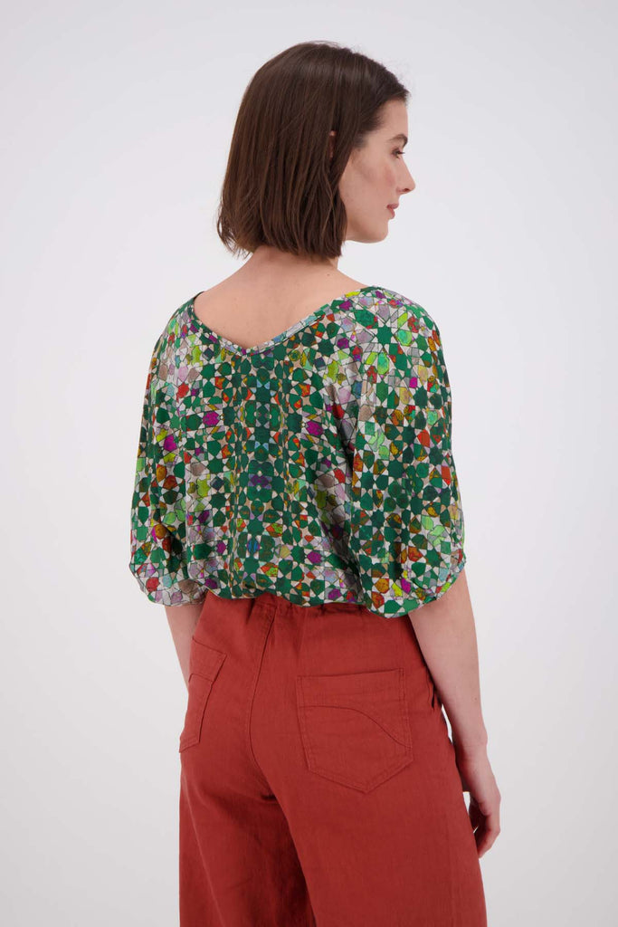 Olga de Polga Kaleidoscope Green Camisa Blouse in printed fine Tencel. This is a reversible top with the choice of a soft V-neck and a boat neck which are interchangeable. Half length sleeves. Finishes at the hip. Back close up view on model.