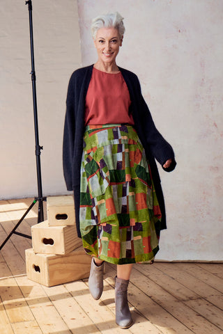 Olga de Polga Sage green Kismet printed Milwaukee skirt in fine cord. Large patch pockets. Unique panelled design. Back elasticated waistband. Front view, worn with a navy knit cardigan.