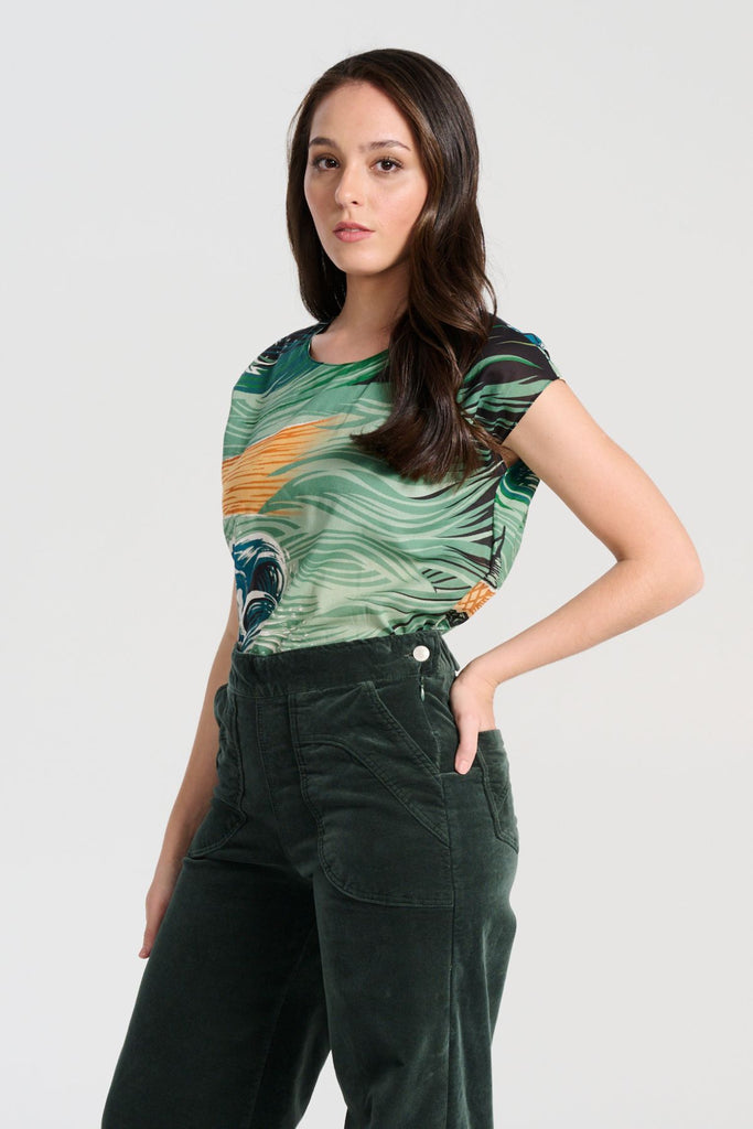 Olga de Polga Isla tee in Tide green printed cotton voile. With cap sleeves, a round neckline with a button fastening at the back neck, tapering in at the waist and finishing at the hip, this tee is perfect for all occasions. Side front view on model