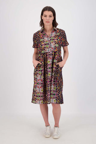 Olga de Polga Grey Kaleidoscope printed Villa dress in long length. Shirt dress with a button front. Finishes just below the knee. 100% Cotton. Front view with hands in pockets on model.