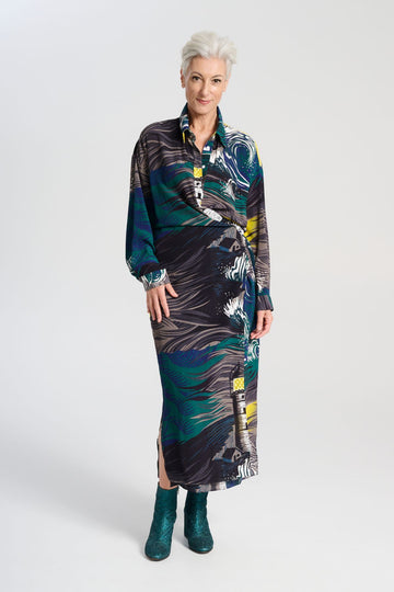 Olga de Polga Fluido wrap shirt dress. Printed Viscose. The Isla print captures the power of nature, with crashing waves and a guiding lighthouse. Deep blues, stormy greens, and yellow accents evoke hope and direction through turbulent times, reflecting the challenges of life and the human drive to navigate the unknown.
Front view on model.