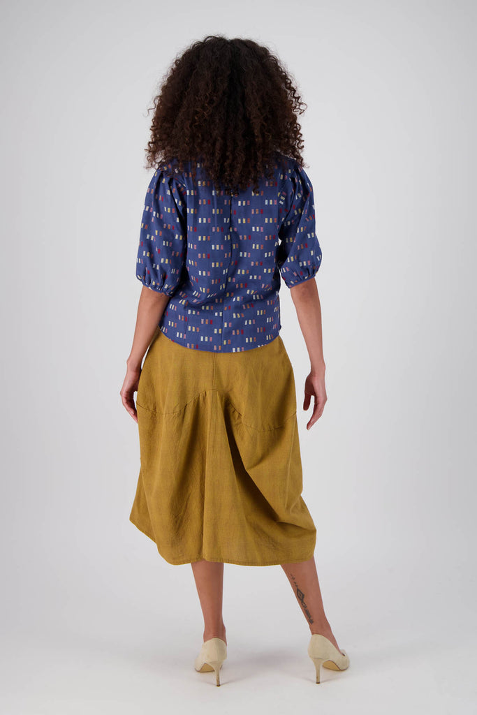 Olga de Polga Milwaukee Textured cotton skirt in Mustard. Best selling chic skirt in a unique cut with large patch pockets and an elasticated back waistband. Midi length. 100% Cotton. Back full length view on model