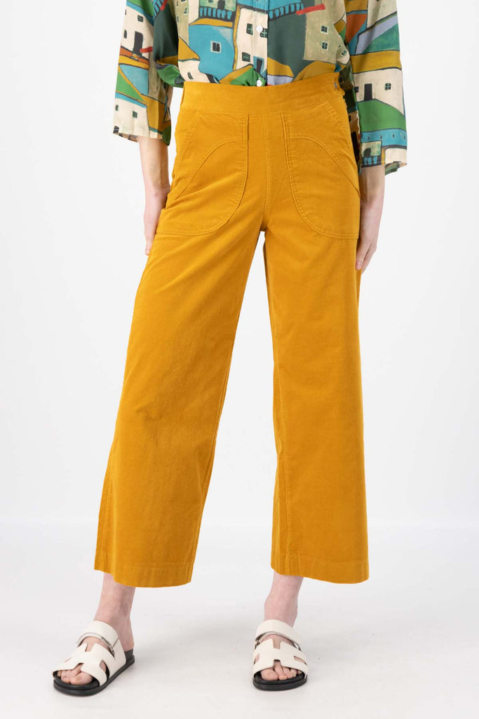 Olga de Polga Peggy Pants in Mustard Yellow fine cotton cord. Cropped length, large front patch pockets, elasticated waistband, side zip fastening. Front close-up view on model.