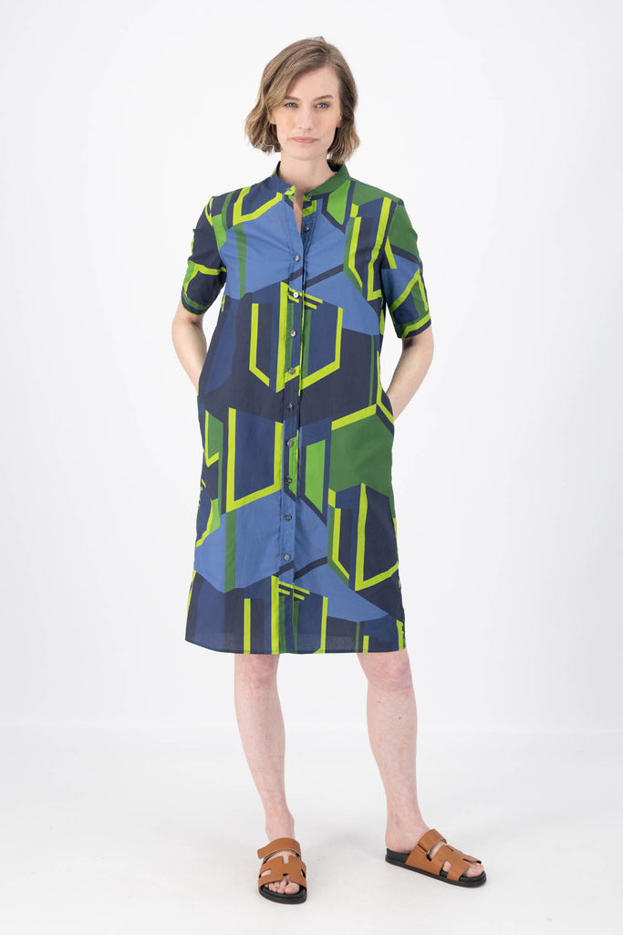 Olga de Polga Plaza dress in navy/green printed cotton. With a large abstract geometric print. 200% Cotton. Short sleeves. Collarless with a front button opening. Knee length. Front view on model.