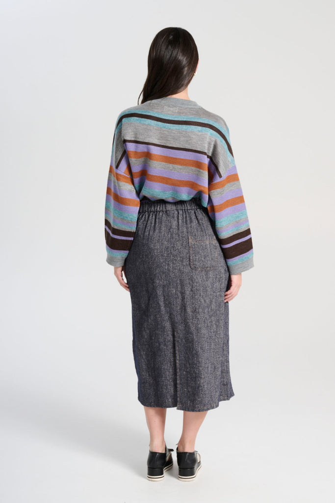 Olga de Polga Navy Hepburn Haven skirt in a wool/linen fabric blend. Featuring a unique button detail at the waist that forms a flattering pocket shape, this skirt adds personality to any outfit. With an elasticated back waist for comfort, it finishes just below the knee and has a stylish back split for ease of movement.  Back view on model.