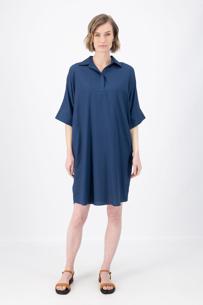 Olga de Polga Marianna Estilo dress in Navy. Shirt dress with bat-wing sleeves and a collar with short button opening at the front. Finishes above the kneed depending on height. Front view on model.