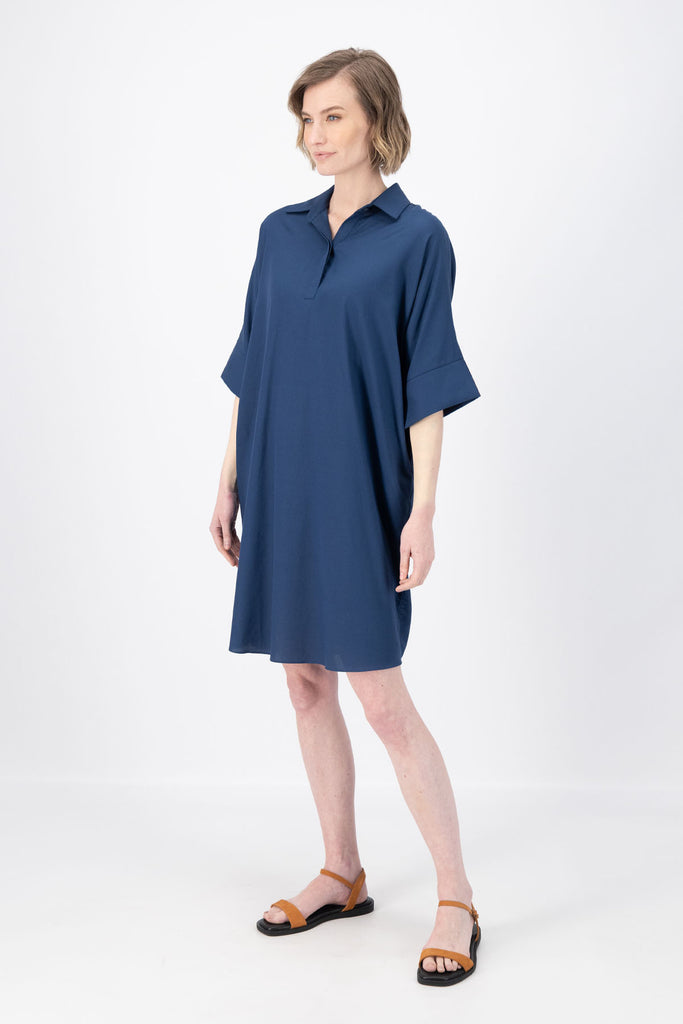 Olga de Polga Marianna Estilo dress in Navy. Shirt dress with bat-wing sleeves and a collar with short button opening at the front. Finishes above the kneed depending on height. Side view on model.