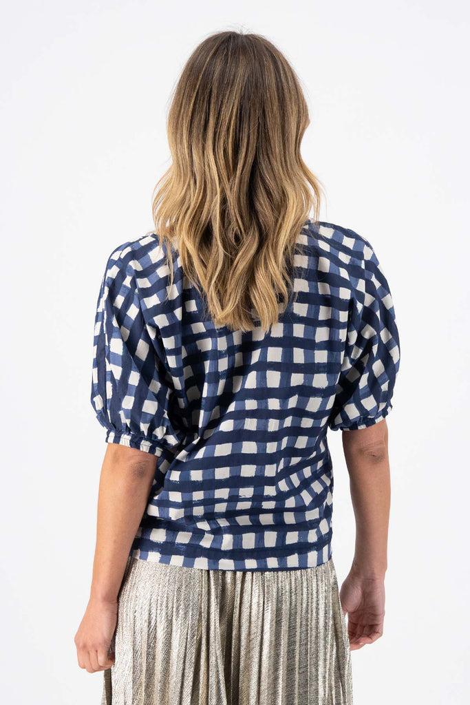 Olga de Polga Camisa blouse in the Rosa Navy print. Printed woven cotton. 100% Cotton. Reversible top to have either a boatneck or a soft V-neckline. Half sleeves with elasticated cuff. Back view on model.