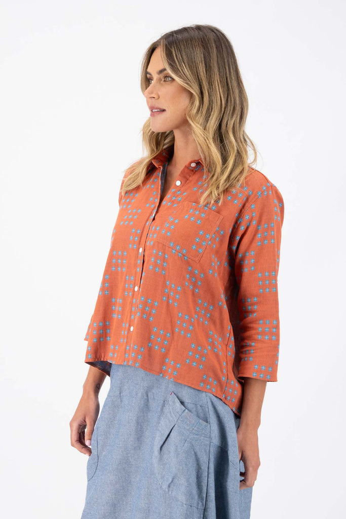 Olga de Polga Network printed cotton shirt in orange with a button down front and collar. 3/4 length sleeves with a foldable sleeve and button fastening. Side view on model.