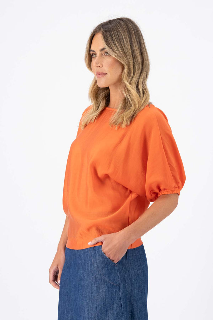 Olga de Polga Camisa Blouse in Orange Skyscraper Tencel. Reversible top with a soft v-neck on one side and a boat neck on the other. Side view on model.