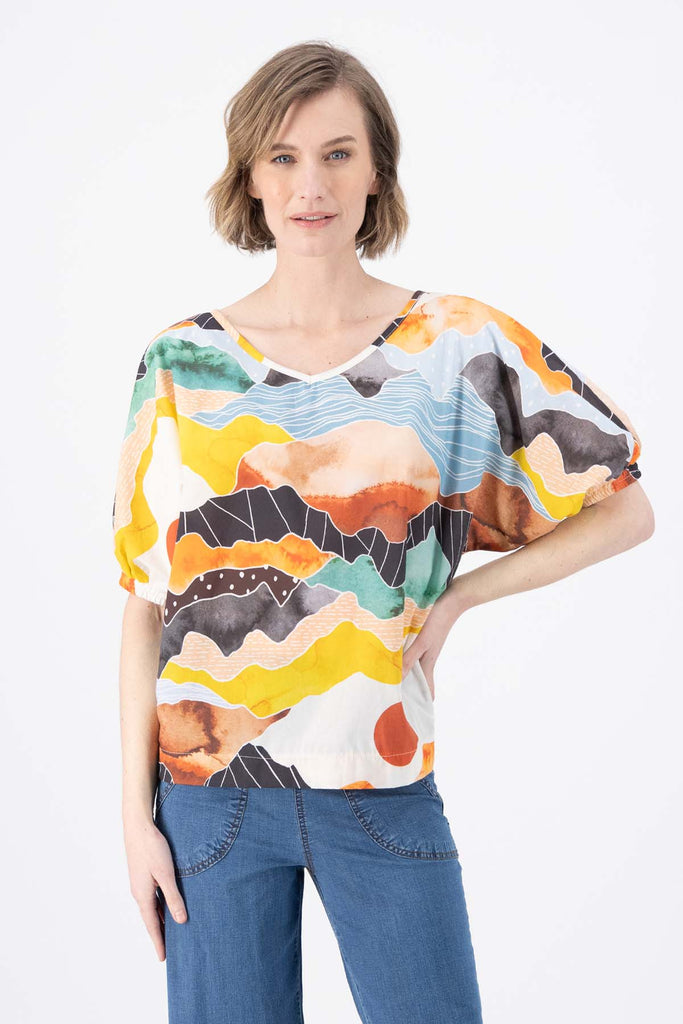 Olga de Polga Orange Vista printed cotton Camisa. Blouse. Reversible top with a soft v-neck on one side and a boat-neck on the other.
Half sleeves, with a bat-wing shape, and tapers in at the hips. Front close up view on model.