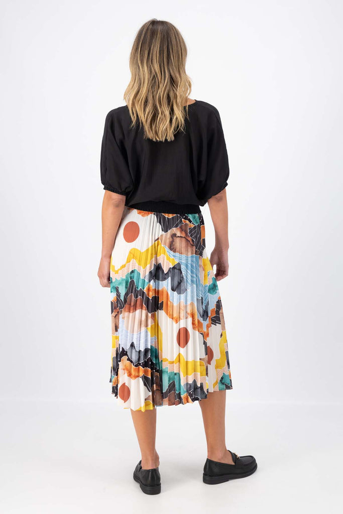 Olga de Polga pleated skirt in the Orange Vista print. Elasticated waistband. Vibrant unique print. Midi length. Back full view on model.