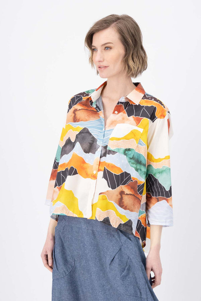 Olga de Polga Orange Vista printed shirt in 100% Cotton. Collar and button down front. 3/4 sleeves. Hip length. Finishes longer at the back. Side view on model.