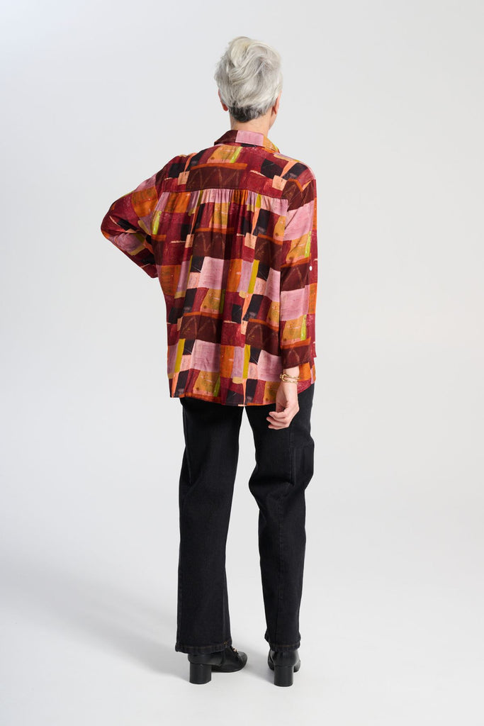 Olga de Polga classic shirt in printed viscose. Kismet Blush Print. Button down front, 3/4 sleeves and a front patch pocket. Print has colours of red, pink, burgundy and accents of yellow and orange. Back view on model