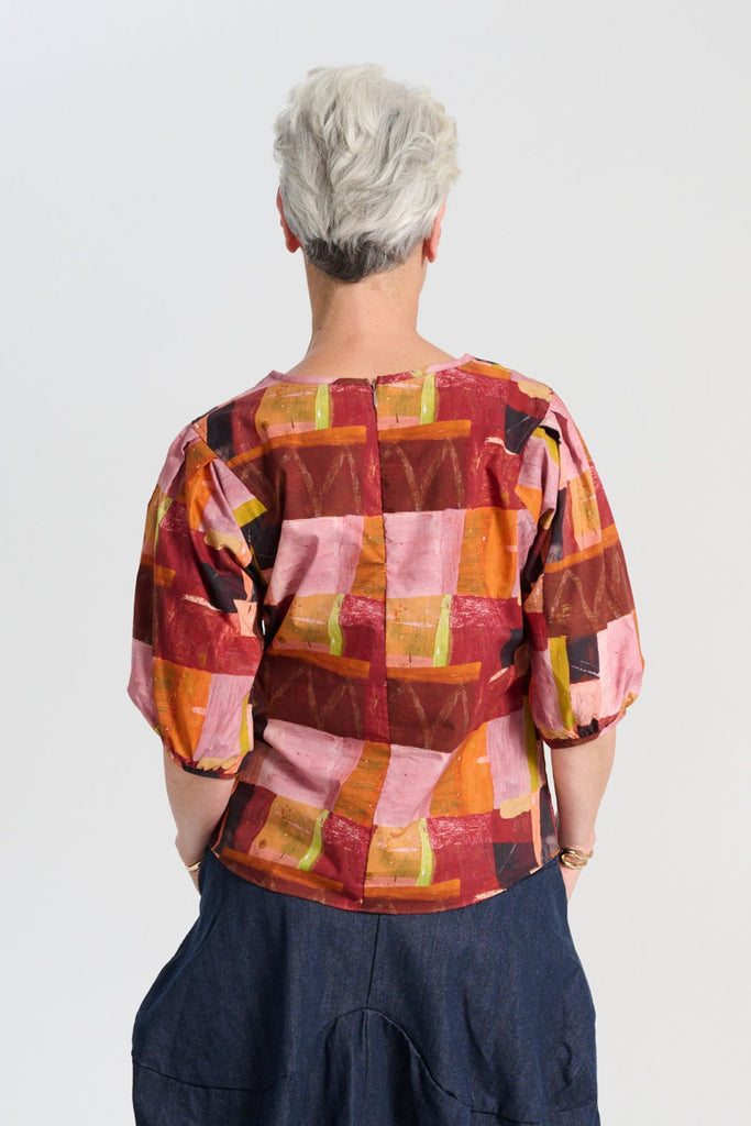 Olga de Polga classic printed blouse in Kismet Blush print. Pinks, reds and burgundy with accents of yellow and orange. Round neckline and lantern shaped sleeves. Back view on model