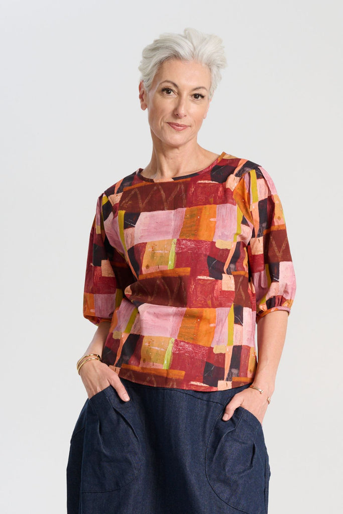 Olga de Polga classic printed blouse in Kismet Blush print. Pinks, reds and burgundy with accents of yellow and orange. Round neckline and lantern shaped sleeves. Front close-up view on model.