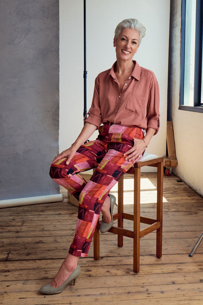 Olga de Polga Printed Pantalon pants in Kismet Blush.  Side front view on model sitting on a chair.